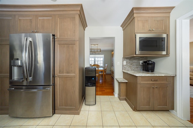 kitchen with stainless steel fridge, light stone countertops, built in microwave, backsplash, and light tile patterned flooring