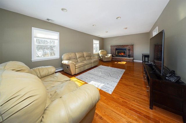 living area featuring visible vents, a baseboard heating unit, a brick fireplace, wood finished floors, and baseboards