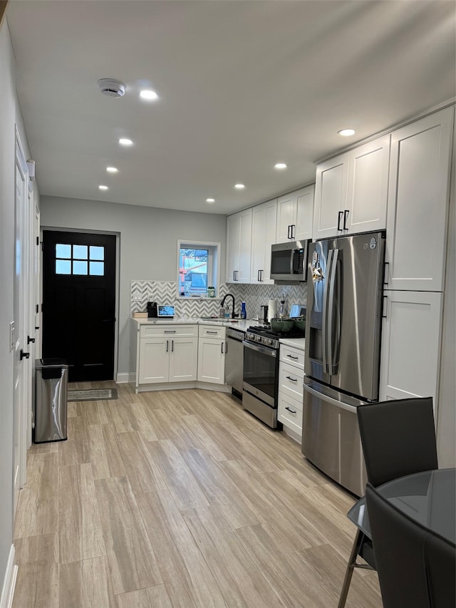 kitchen with white cabinetry, backsplash, stainless steel appliances, and light hardwood / wood-style floors