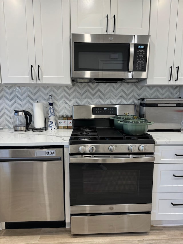 kitchen with white cabinetry, light wood-type flooring, stainless steel appliances, light stone countertops, and decorative backsplash