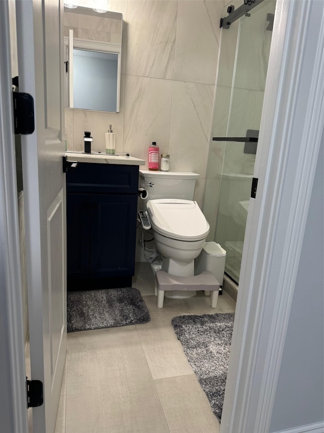 bathroom with toilet, a shower with shower door, tile walls, vanity, and tile patterned flooring