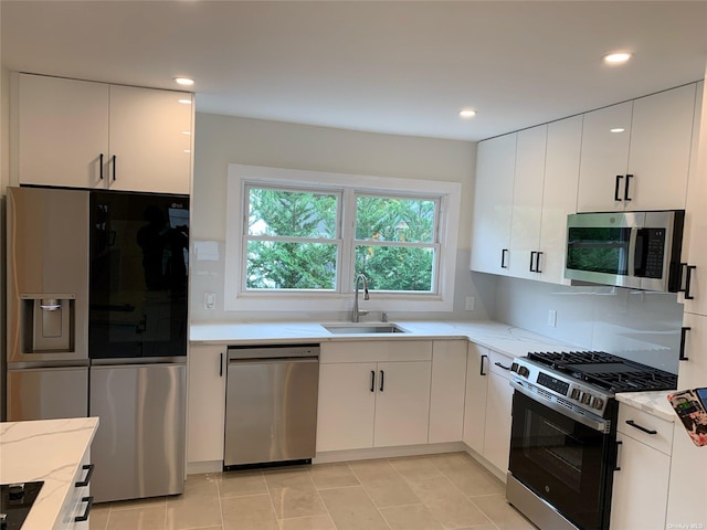 kitchen with sink, light tile patterned floors, appliances with stainless steel finishes, white cabinetry, and light stone countertops