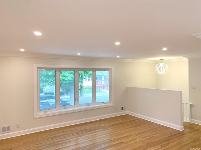 spare room featuring ornamental molding, wood-type flooring, and a notable chandelier