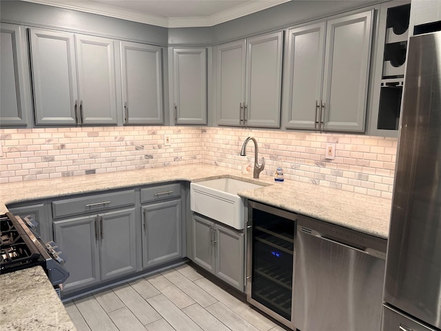 kitchen with gray cabinets, appliances with stainless steel finishes, backsplash, light stone countertops, and beverage cooler