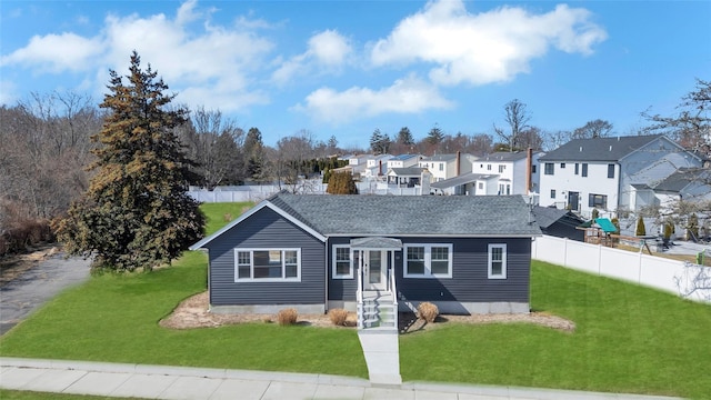 view of front of house featuring a residential view, fence, a front lawn, and roof with shingles