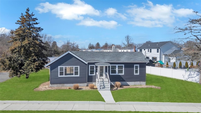 view of front of house featuring a shingled roof, a front yard, and fence