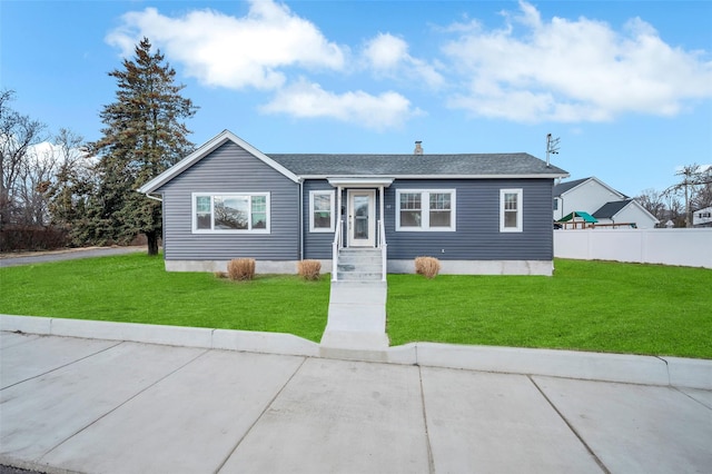 view of front facade featuring a shingled roof, a front yard, and fence