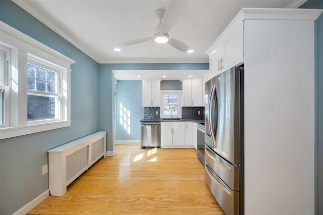 kitchen with stainless steel appliances, white cabinetry, light wood-type flooring, backsplash, and radiator heating unit