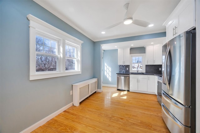 kitchen featuring stainless steel appliances, baseboards, backsplash, light wood finished floors, and radiator heating unit