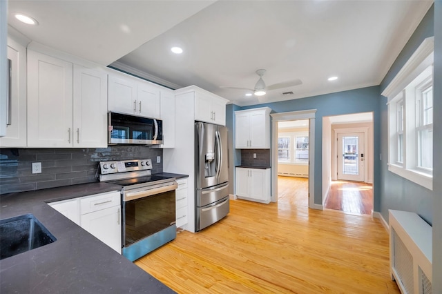 kitchen featuring tasteful backsplash, white cabinets, dark countertops, light wood-style flooring, and appliances with stainless steel finishes