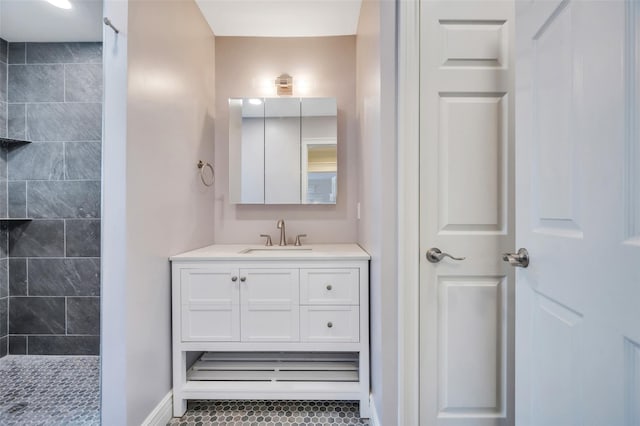 bathroom featuring a tile shower, vanity, and baseboards