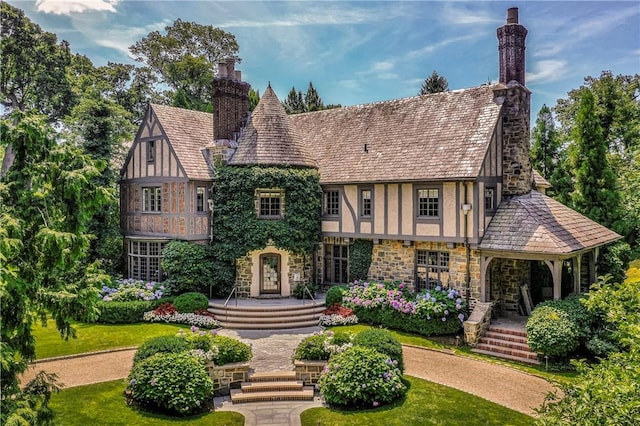 tudor-style house featuring stone siding, stucco siding, a chimney, and covered porch