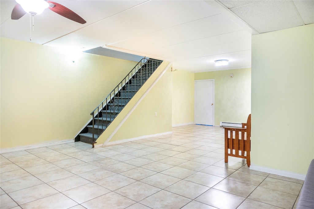 tiled empty room with ceiling fan and baseboard heating