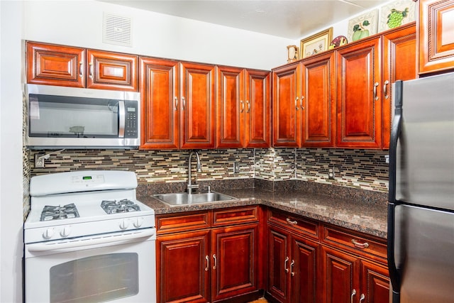 kitchen with sink, backsplash, dark stone counters, and appliances with stainless steel finishes