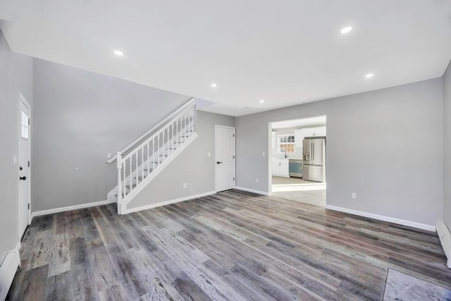 unfurnished living room with wood-type flooring, a healthy amount of sunlight, and baseboard heating