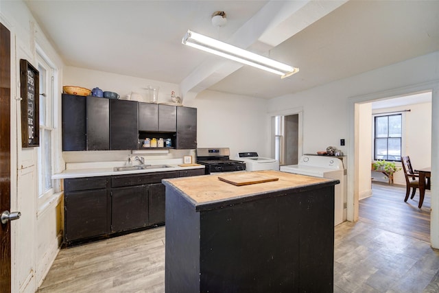 kitchen featuring a kitchen island, sink, independent washer and dryer, stainless steel gas range oven, and light wood-type flooring