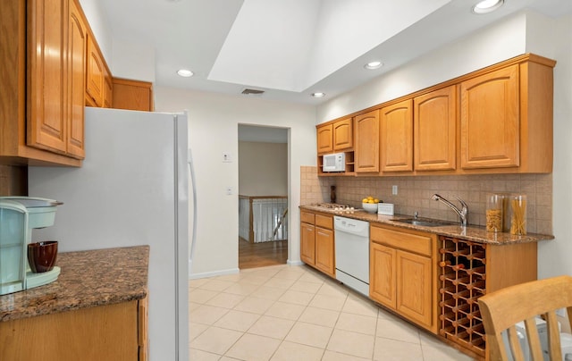 kitchen with sink, white appliances, light tile patterned floors, dark stone countertops, and decorative backsplash