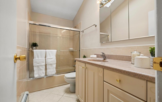 full bathroom with tile walls, a baseboard heating unit, bath / shower combo with glass door, vanity, and toilet