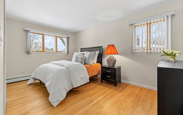 bedroom with baseboard heating, multiple windows, and light hardwood / wood-style flooring