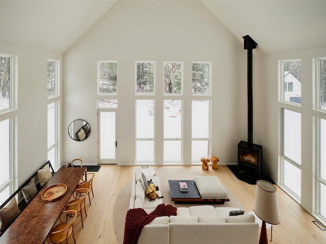 living room featuring high vaulted ceiling, a wood stove, a wealth of natural light, and light hardwood / wood-style floors