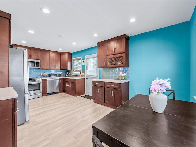 kitchen with stainless steel appliances, sink, backsplash, and light hardwood / wood-style flooring