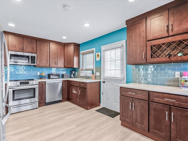 kitchen with tasteful backsplash, stainless steel appliances, sink, and light wood-type flooring