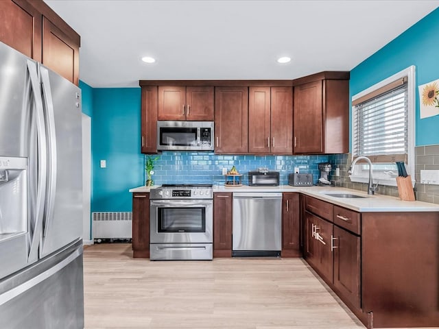 kitchen featuring radiator, sink, decorative backsplash, stainless steel appliances, and light hardwood / wood-style flooring