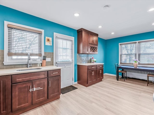 kitchen with radiator heating unit, tasteful backsplash, sink, dark brown cabinets, and light hardwood / wood-style flooring