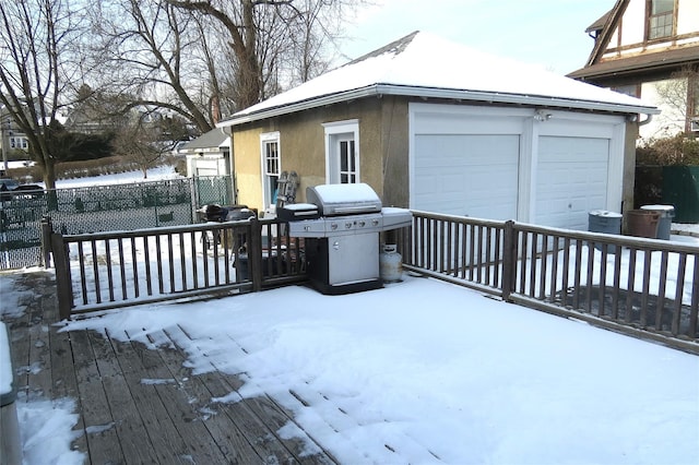 snow covered deck with a garage, an outdoor structure, and area for grilling