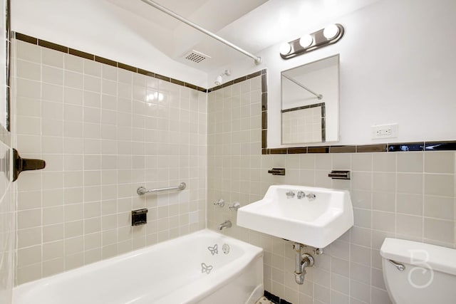 full bathroom featuring toilet, tiled shower / bath combo, sink, and tile walls