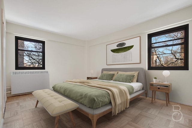 bedroom with multiple windows, radiator, and light parquet flooring