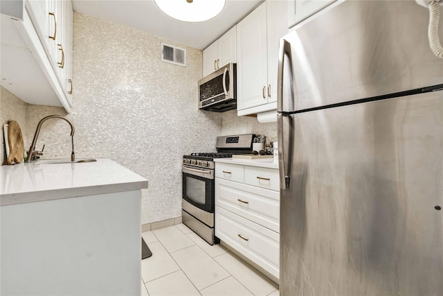 kitchen with light tile patterned flooring, sink, stainless steel appliances, and white cabinetry