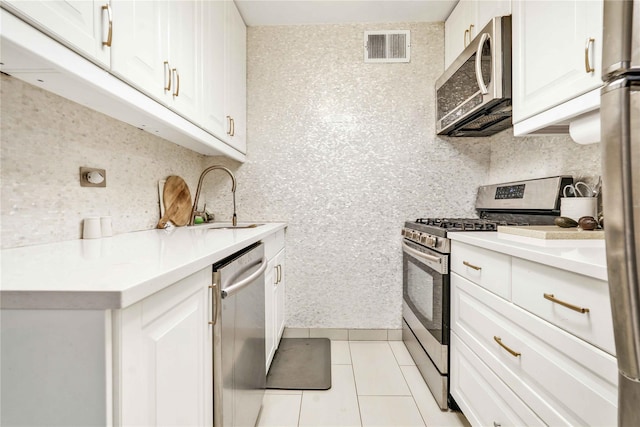 kitchen with tasteful backsplash, stainless steel appliances, white cabinets, light tile patterned flooring, and sink