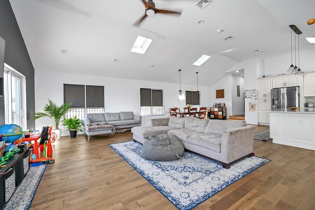 living room with a skylight, high vaulted ceiling, ceiling fan, and light wood-type flooring