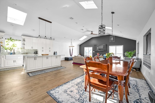 dining area with ceiling fan, sink, vaulted ceiling with skylight, and light wood-type flooring