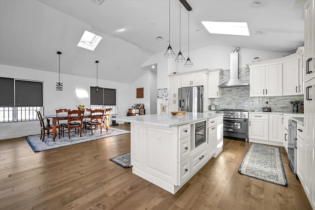 kitchen featuring white cabinetry, a skylight, appliances with stainless steel finishes, a kitchen island, and wall chimney range hood