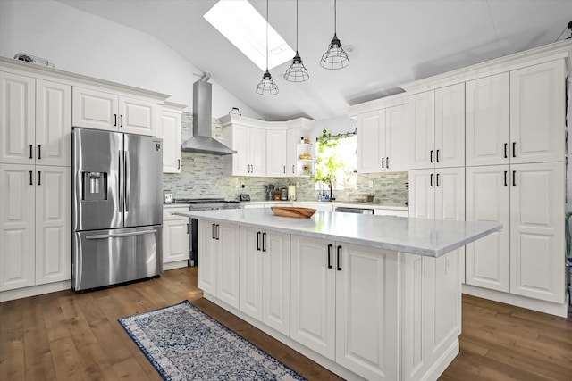 kitchen featuring wall chimney exhaust hood, a kitchen island, pendant lighting, stainless steel appliances, and white cabinets