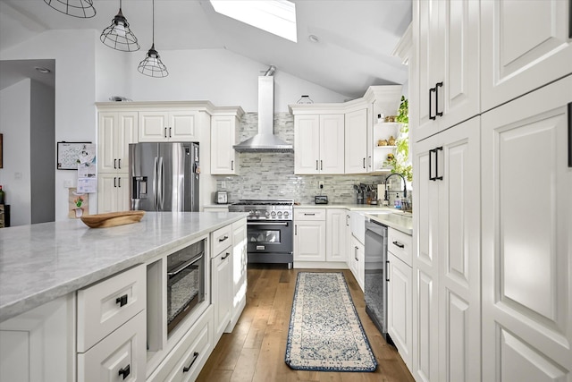 kitchen featuring sink, light stone counters, appliances with stainless steel finishes, wall chimney range hood, and white cabinets