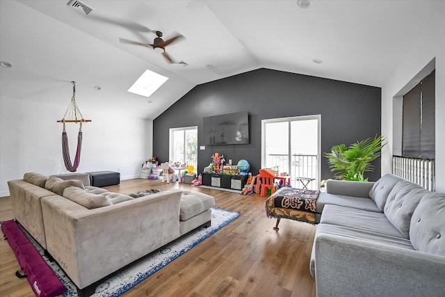 living room featuring ceiling fan, light hardwood / wood-style flooring, and vaulted ceiling with skylight