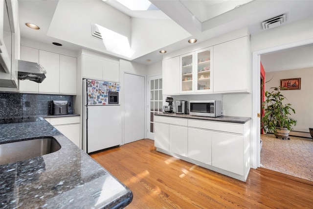 kitchen featuring a skylight, white cabinets, backsplash, white refrigerator with ice dispenser, and light hardwood / wood-style flooring