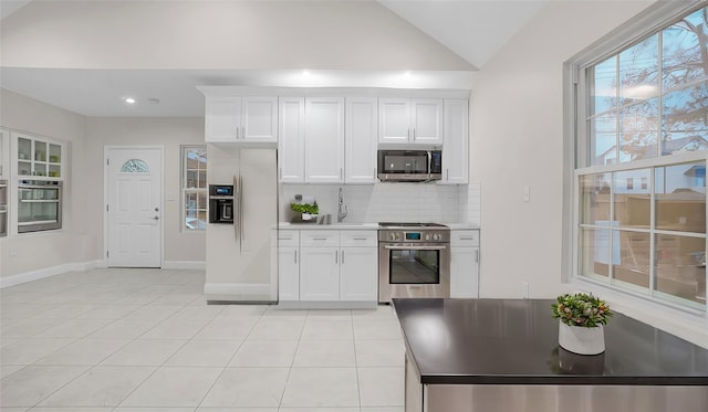 kitchen featuring vaulted ceiling, light tile patterned floors, white cabinets, stainless steel appliances, and backsplash