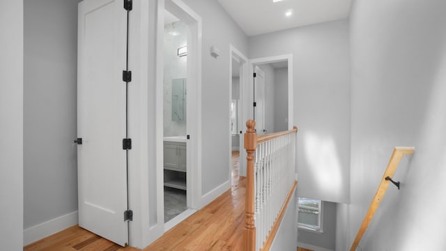 hall with wood finished floors, an upstairs landing, and baseboards