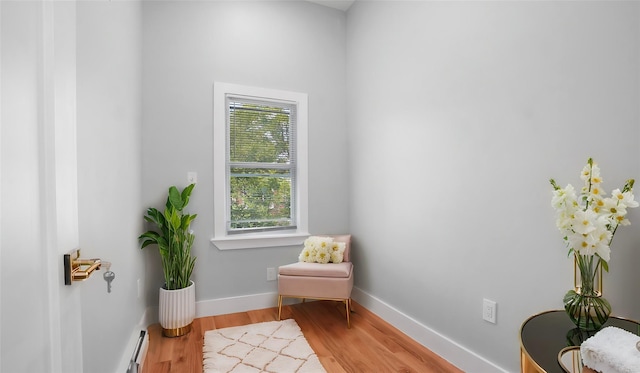 sitting room with a baseboard heating unit, baseboards, and wood finished floors