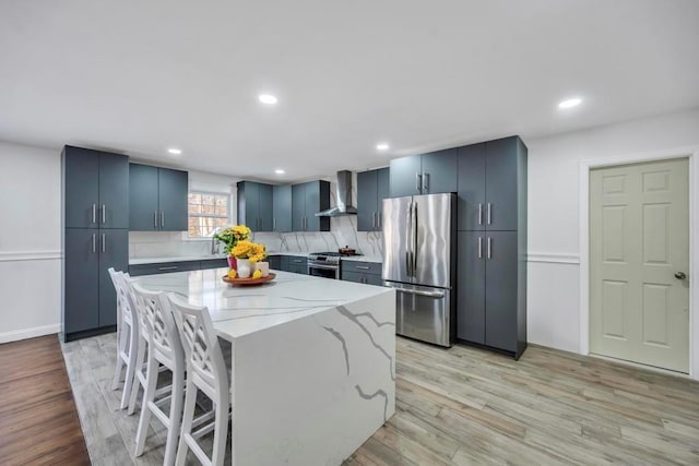 kitchen featuring a kitchen island, appliances with stainless steel finishes, wall chimney range hood, and light hardwood / wood-style flooring