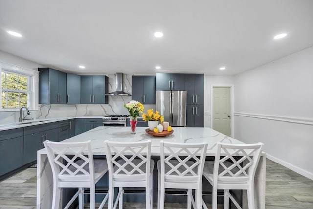 kitchen featuring wall chimney exhaust hood, stainless steel appliances, a kitchen bar, and a center island