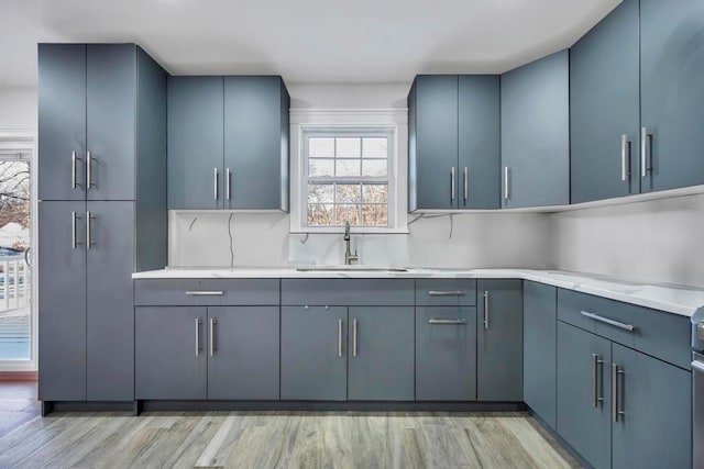 kitchen with backsplash, blue cabinets, sink, and light wood-type flooring