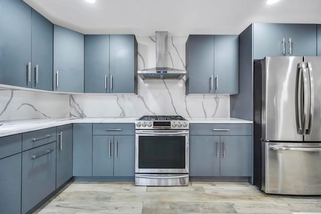 kitchen with wall chimney exhaust hood, stainless steel appliances, blue cabinetry, and backsplash