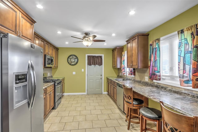 kitchen featuring sink, a breakfast bar area, dark stone countertops, appliances with stainless steel finishes, and ceiling fan