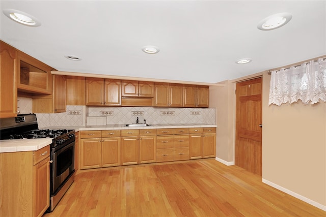 kitchen with sink, tile countertops, stainless steel gas range, and light hardwood / wood-style flooring