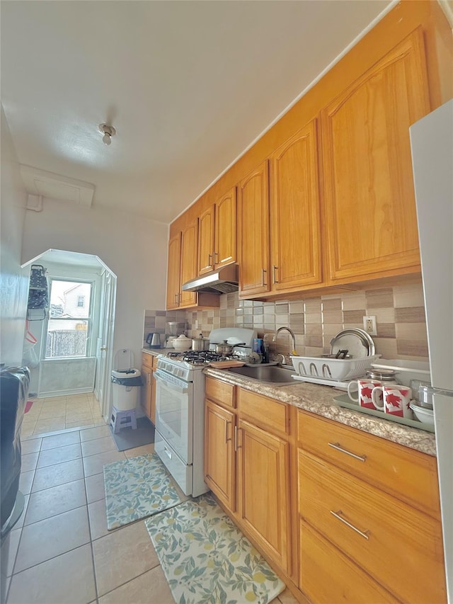 kitchen with tasteful backsplash, sink, white gas stove, and light tile patterned flooring